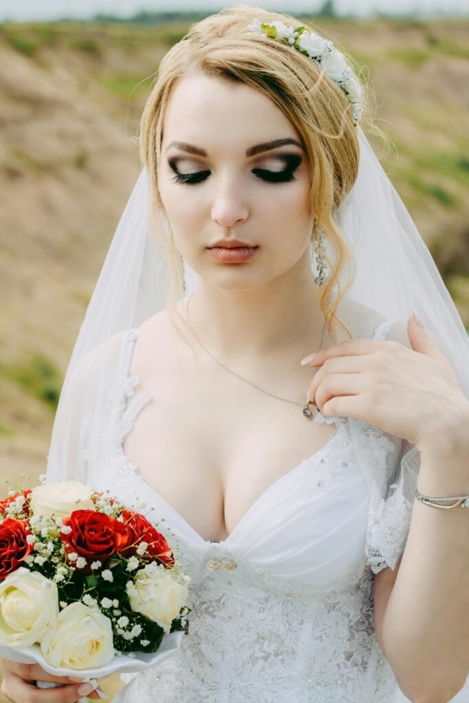 Beautiful bride in a white gown holding a red and white bouquet outdoors.