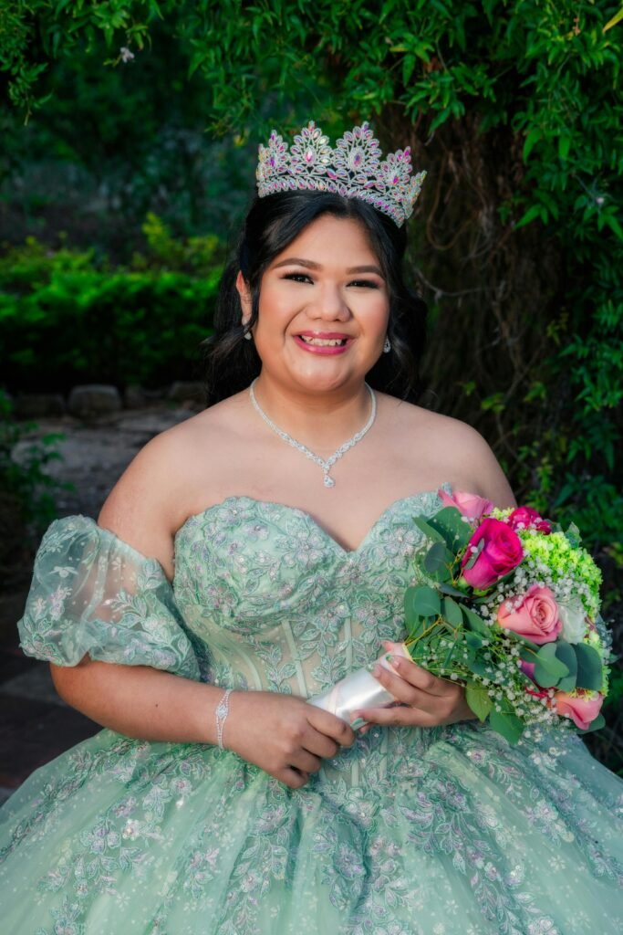 Smiling young woman in ornate gown holding bouquet outdoors.