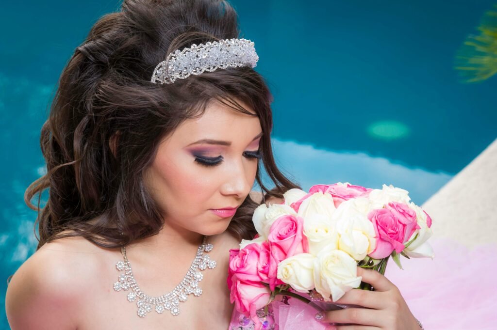 A young woman in a quinceañera gown holding a bouquet of pink and white roses, adorned with a tiara.